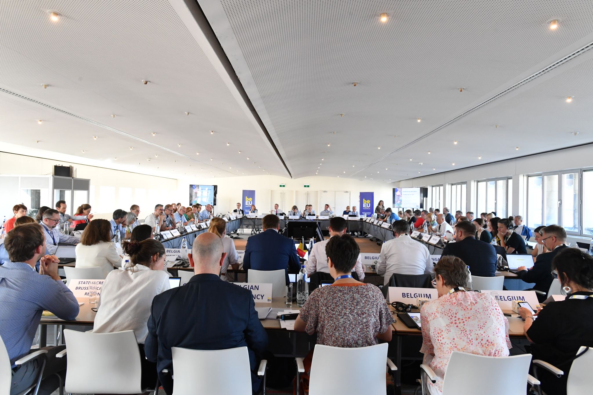 People gather around tables arranged in a square in a meeting room.