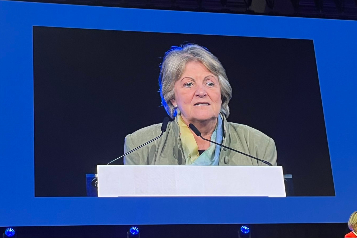 Video of a woman speaking, shown on a large screen