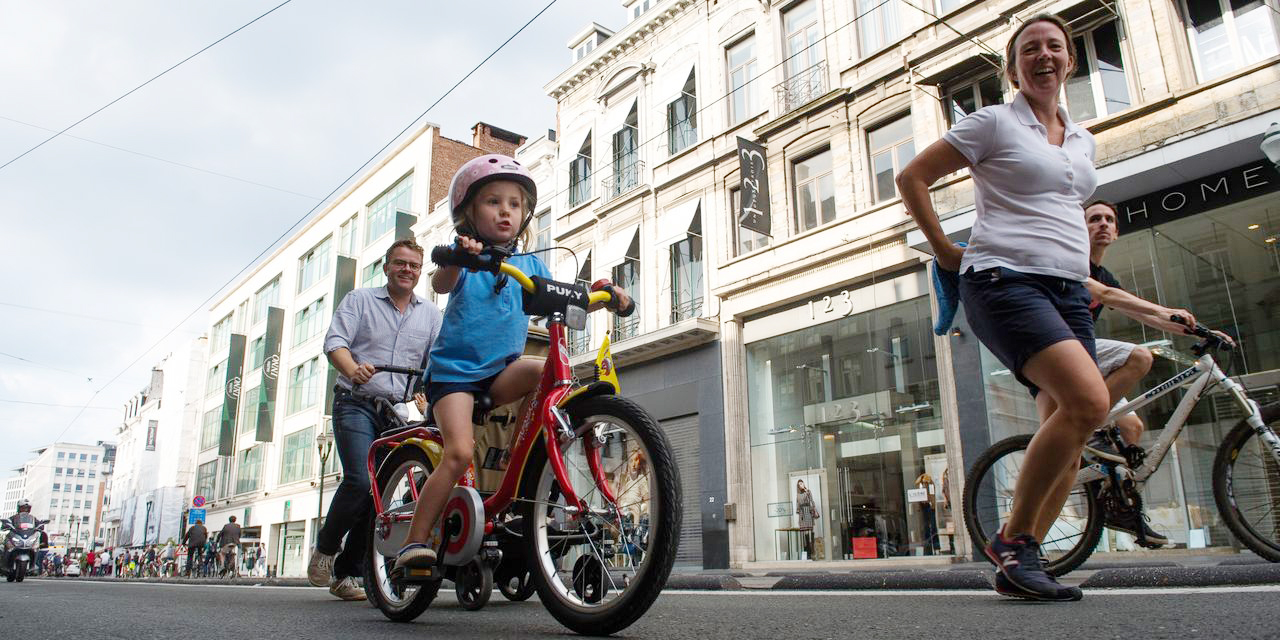 A family on the street, the parents are walking and the children are on their bikes