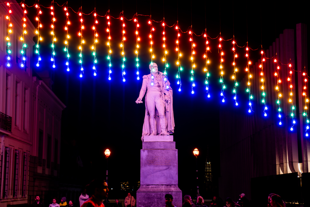Rainbow-coloured light bulbs illuminate a statue.
