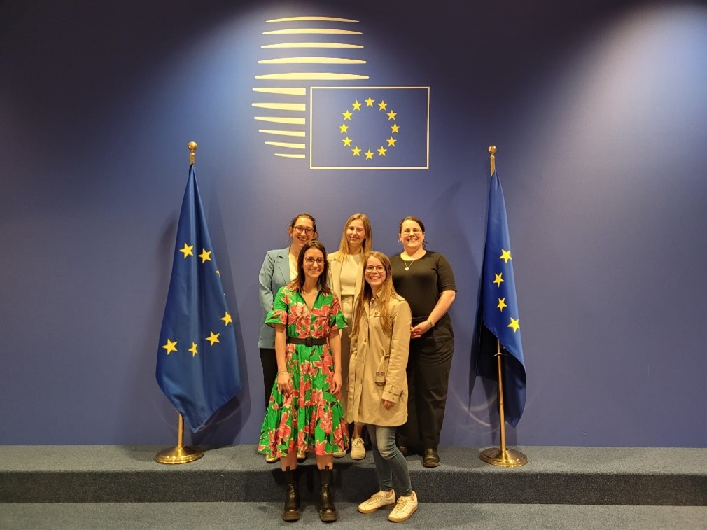 Un groupe de cinq femmes posent entre deux drapeaux européens.