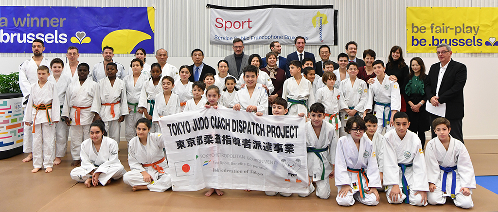 De jonge Brusselse judoka’s en de officiële delegatie poseren met een vlag van het project. 