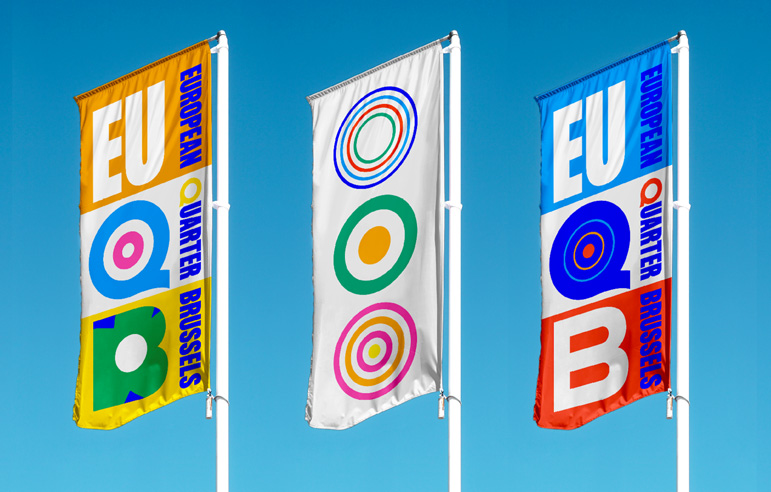 Three colourful flags bearing the new European Quarter brand flutter in the wind under a blue sky.