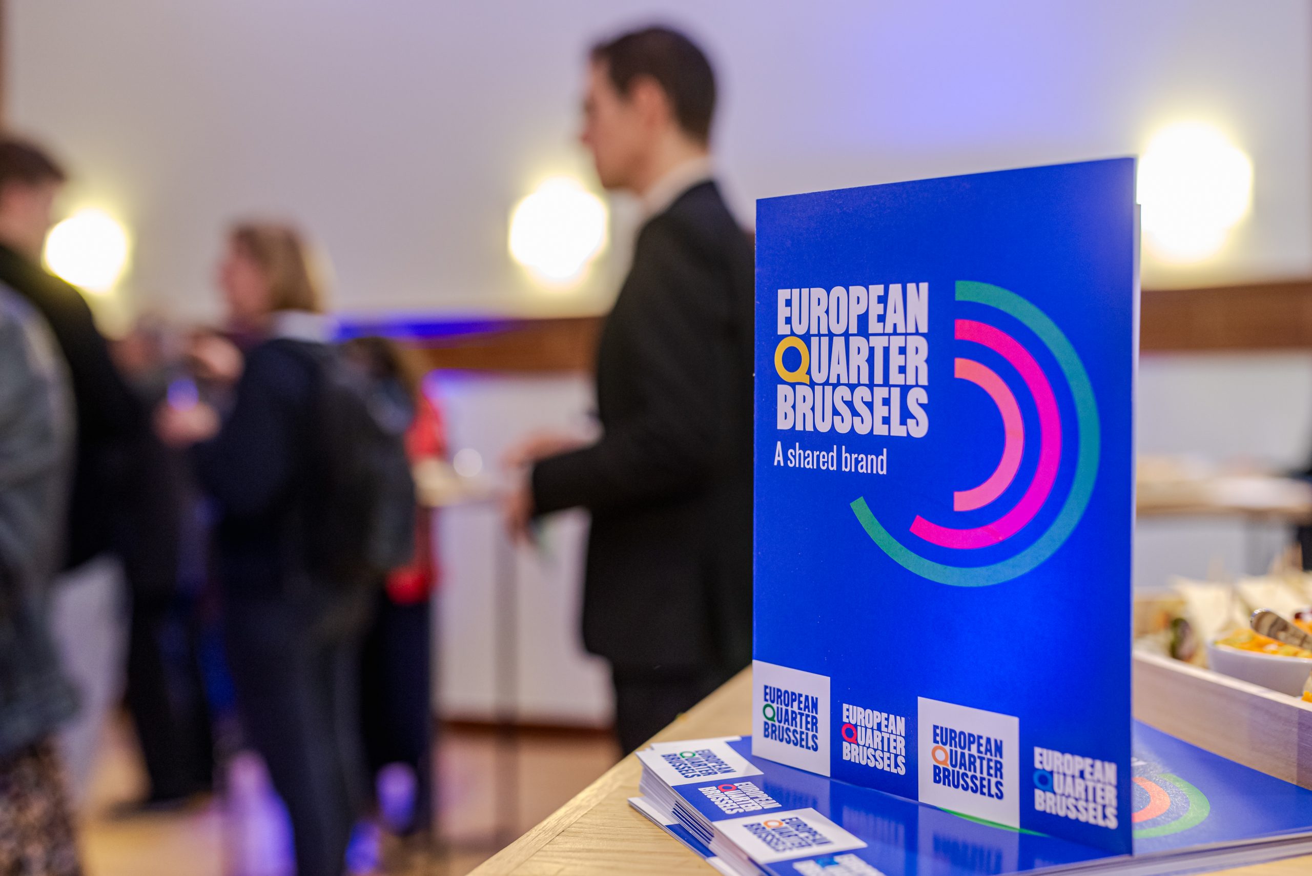 Un panneau bleu avec le nouveau logo du Quartier européen posé sur une table.