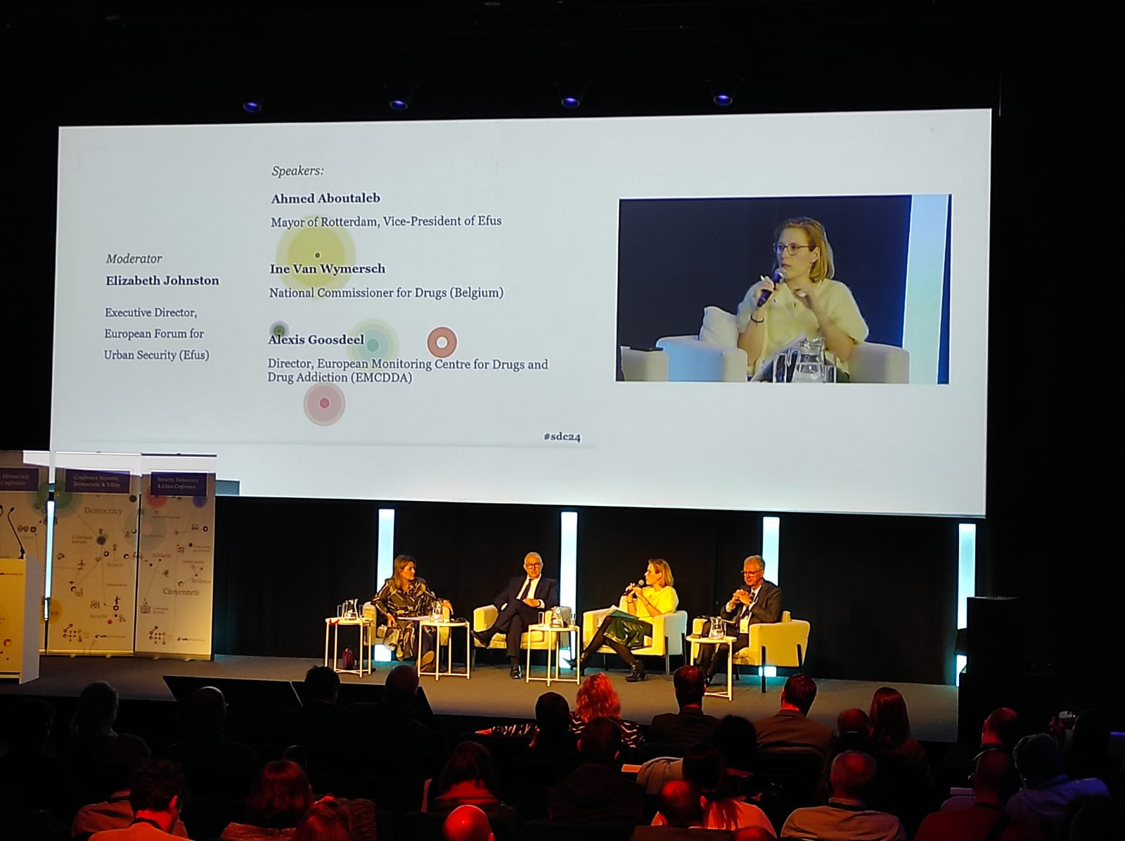 Panelists debate on stage in front of a giant screen.