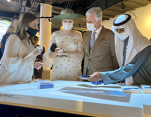 Koning Filip en koningin Mathilde, Ilham Kadri en een deelnemer uit Dubai, staand rond een presentatietafel