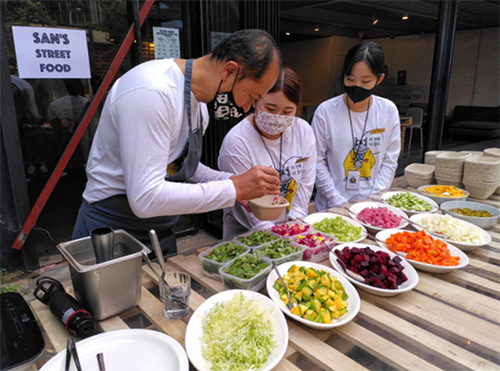 De chef-kok en twee jonge vrouwen achter een stand met streetfood.