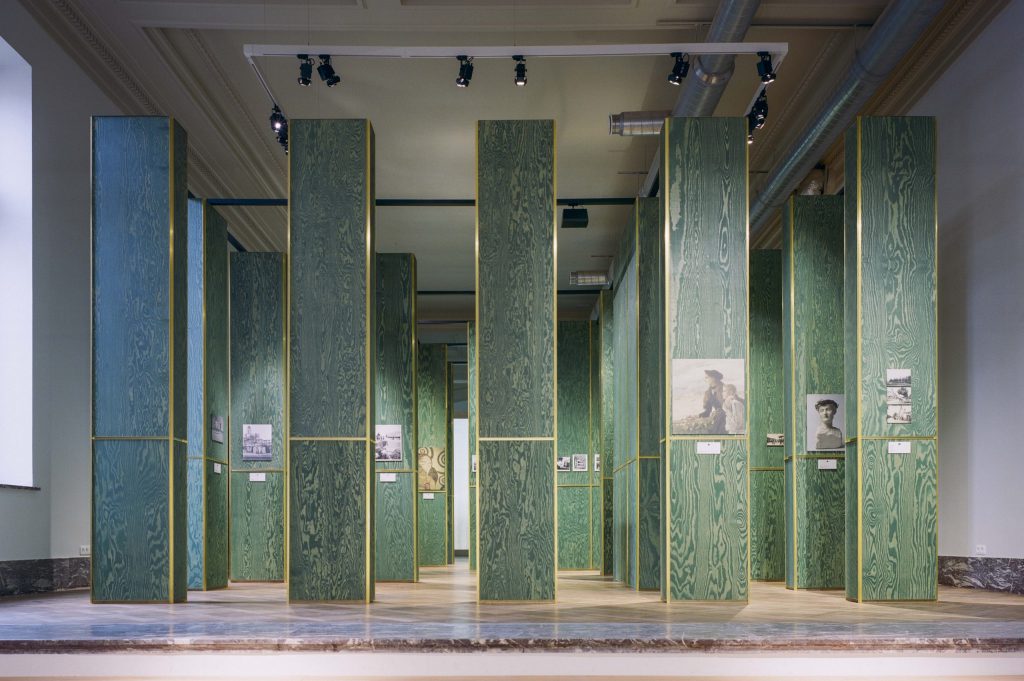 Des photos affichées sur des piliers verts dans une grande salle vide.