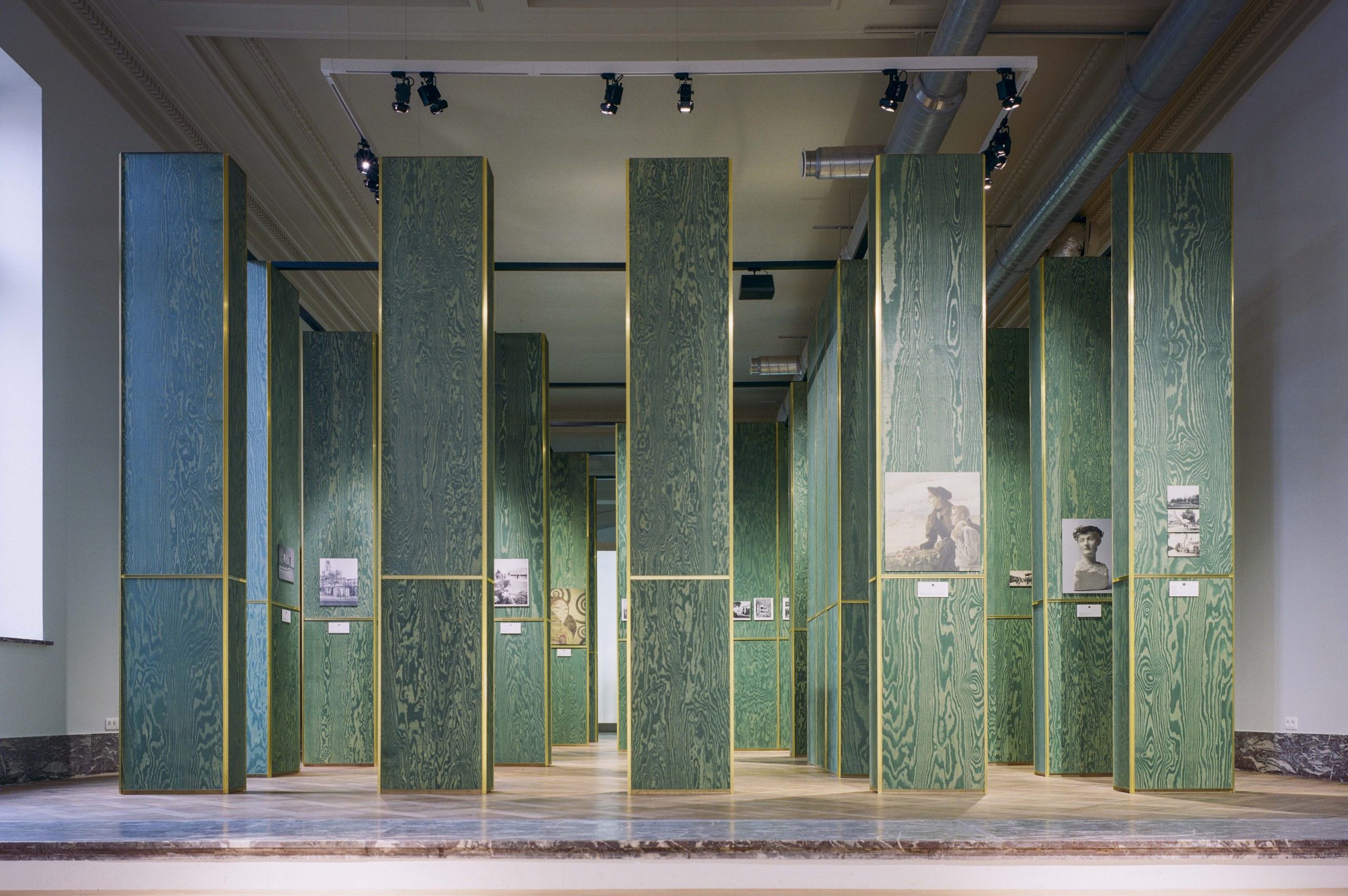 Photos displayed on green pillars in a large empty room.