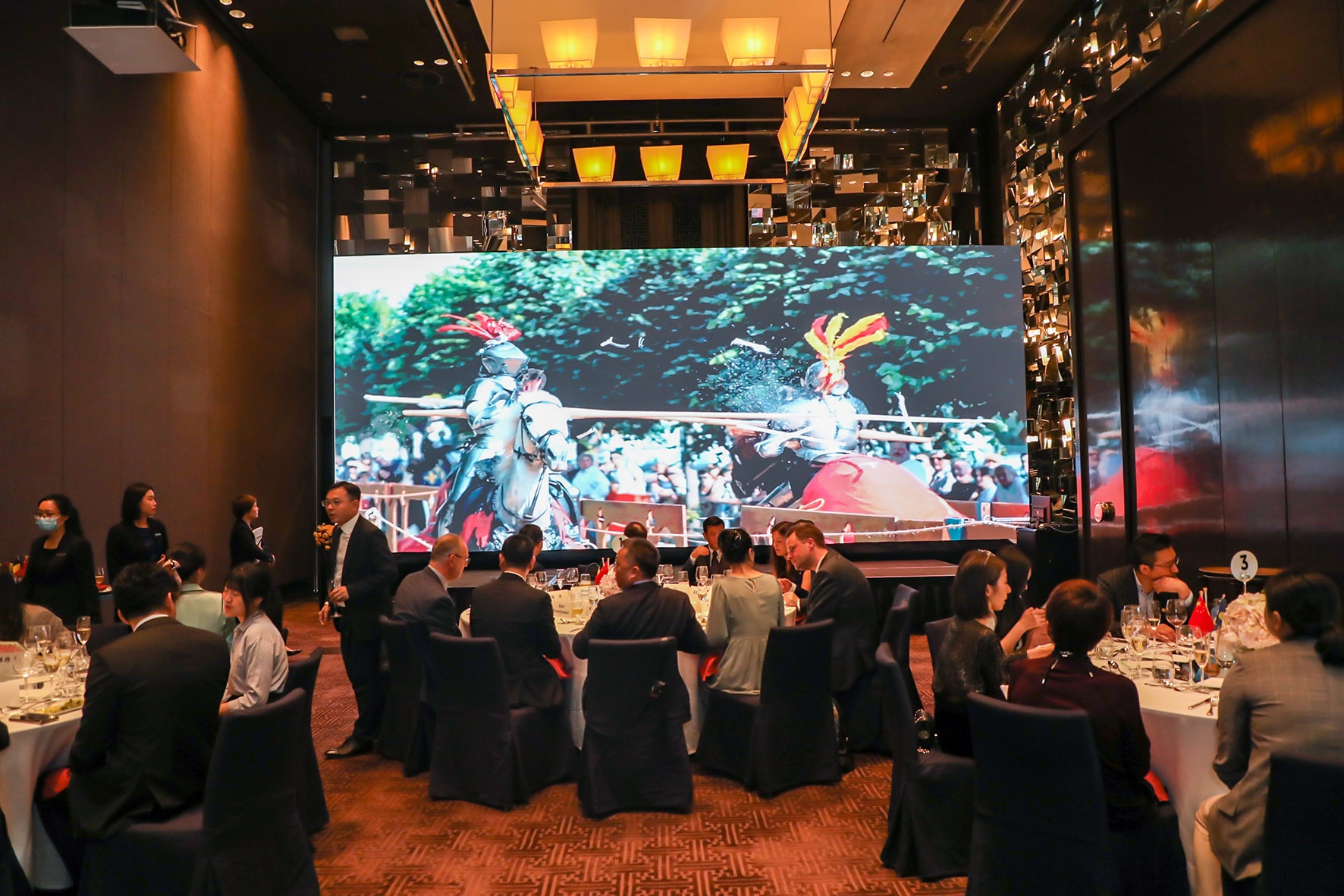 Participants seated at round tables, facing a large screen