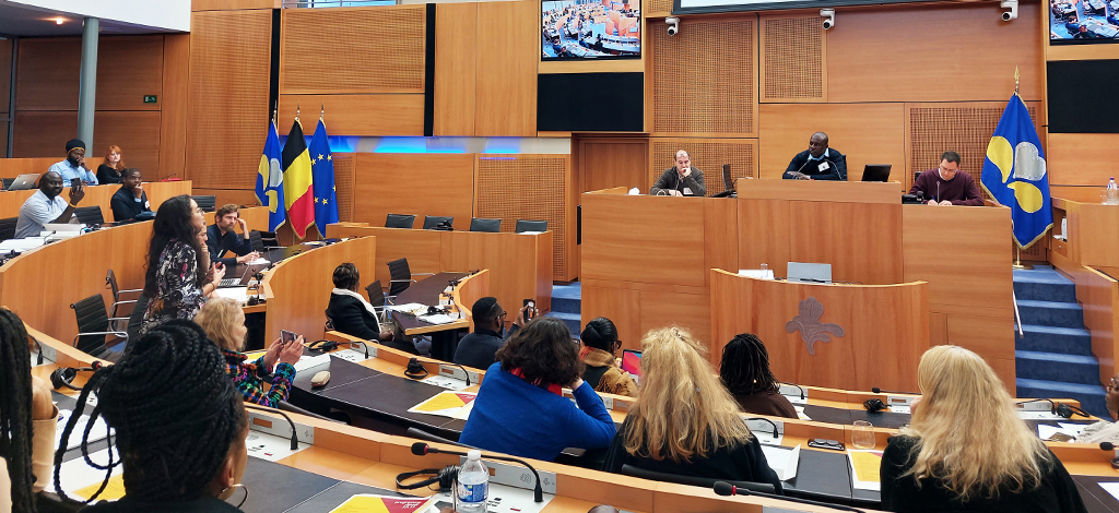 Participants assis face aux orateurs, dans l’hémicycle du Parlement bruxellois