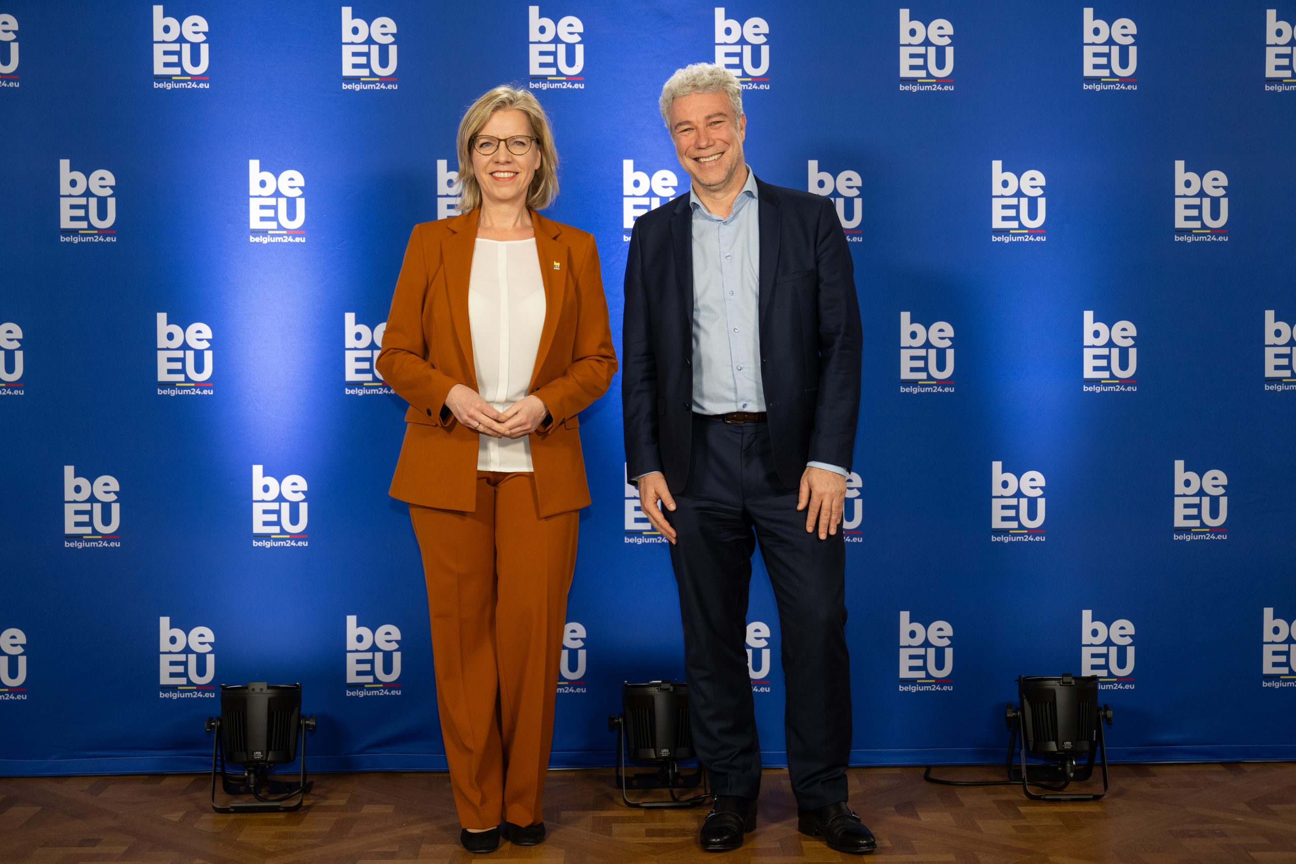 Twee ministers poseren voor een blauwe achtergrond.