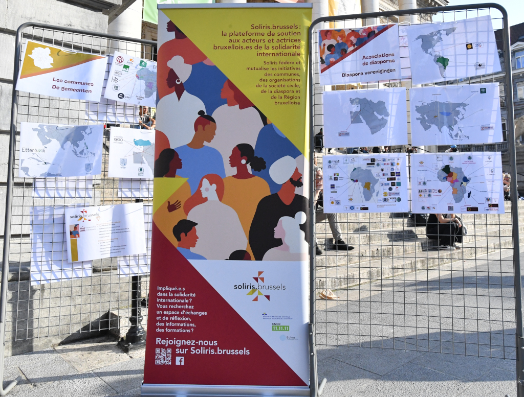 Un stand d'information de Soliris.brussels avec une bannière colorée et des cartes affichées montrant les associations de la diaspora et les communes de Bruxelles.